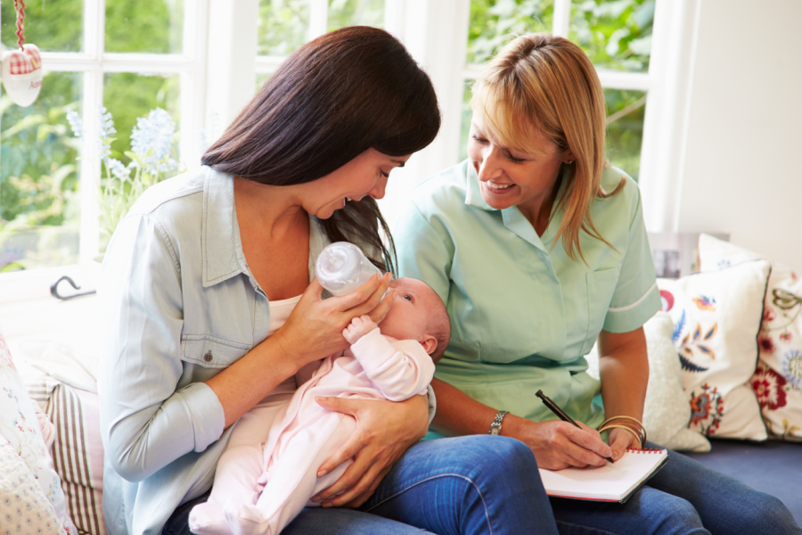 Mother holding newborn and midwife sitting next ot her providing support