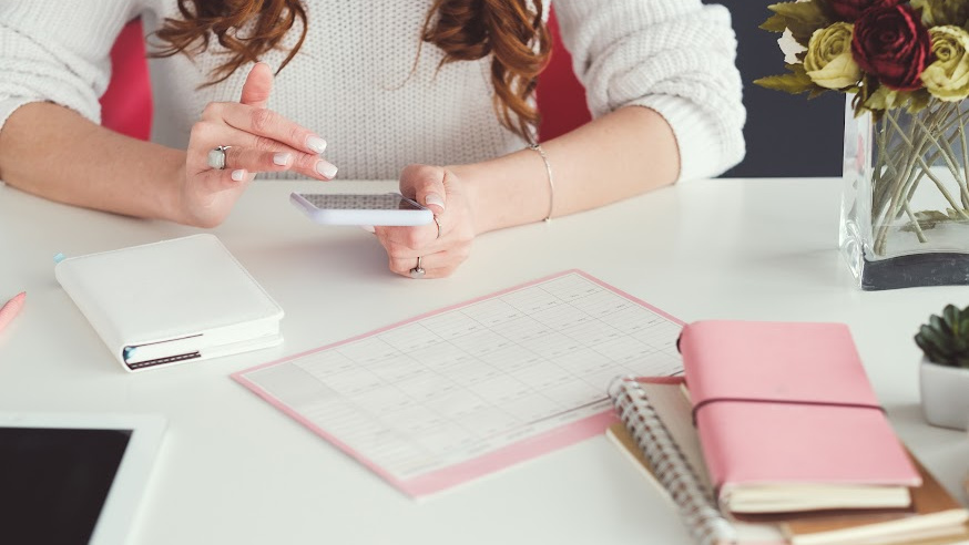 woman sitting at a desk, hands showing her holding a phone and a marketing calendar in front of her