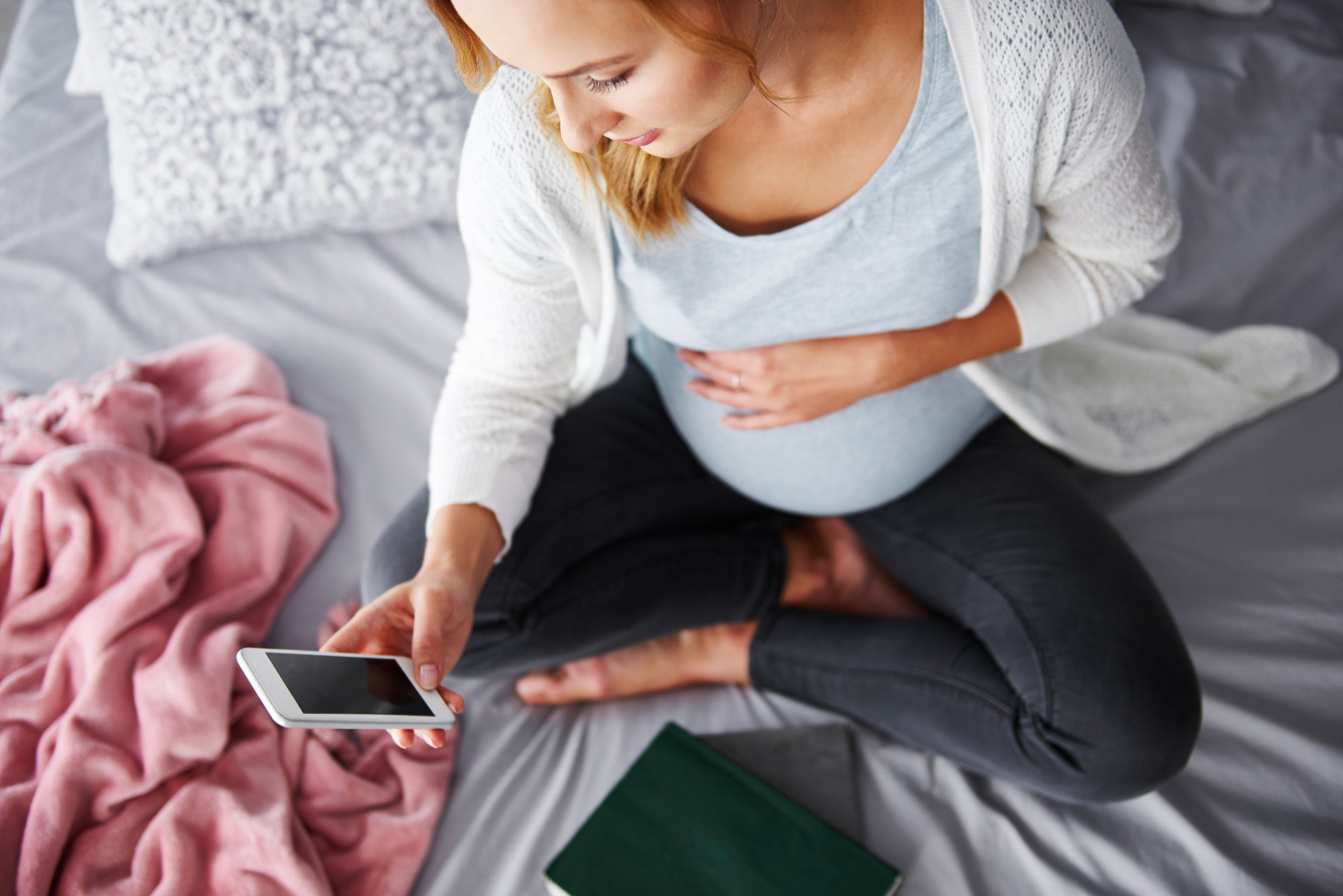 pregnant woman on bed with cell phone